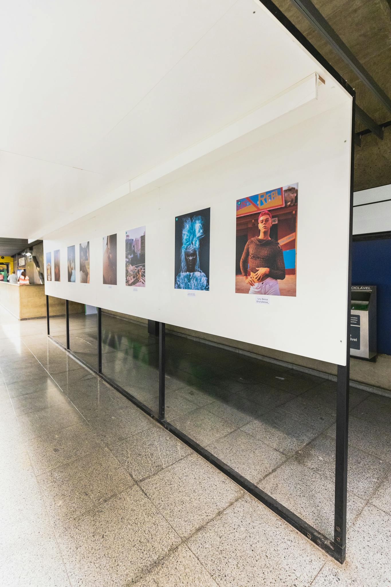 Wide-angle view of an indoor art exhibition with various photographs displayed on a white wall.